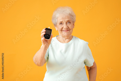 Diabetic senior woman with glucometer on yellow background photo