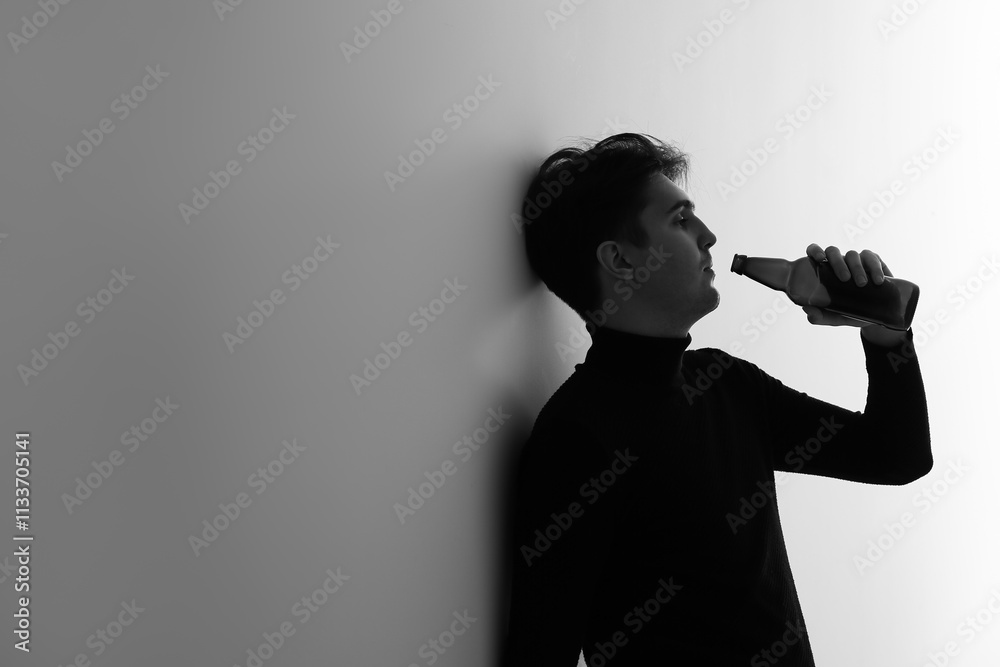 Black and white portrait of depressed young man drinking beer near light wall Black and white portrait of depressed young man drinking beer near light wall