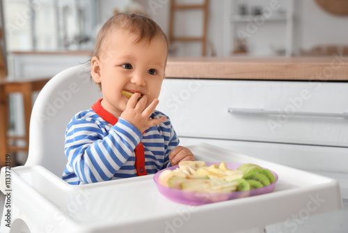 Cute little baby eating fruits in high chair at home