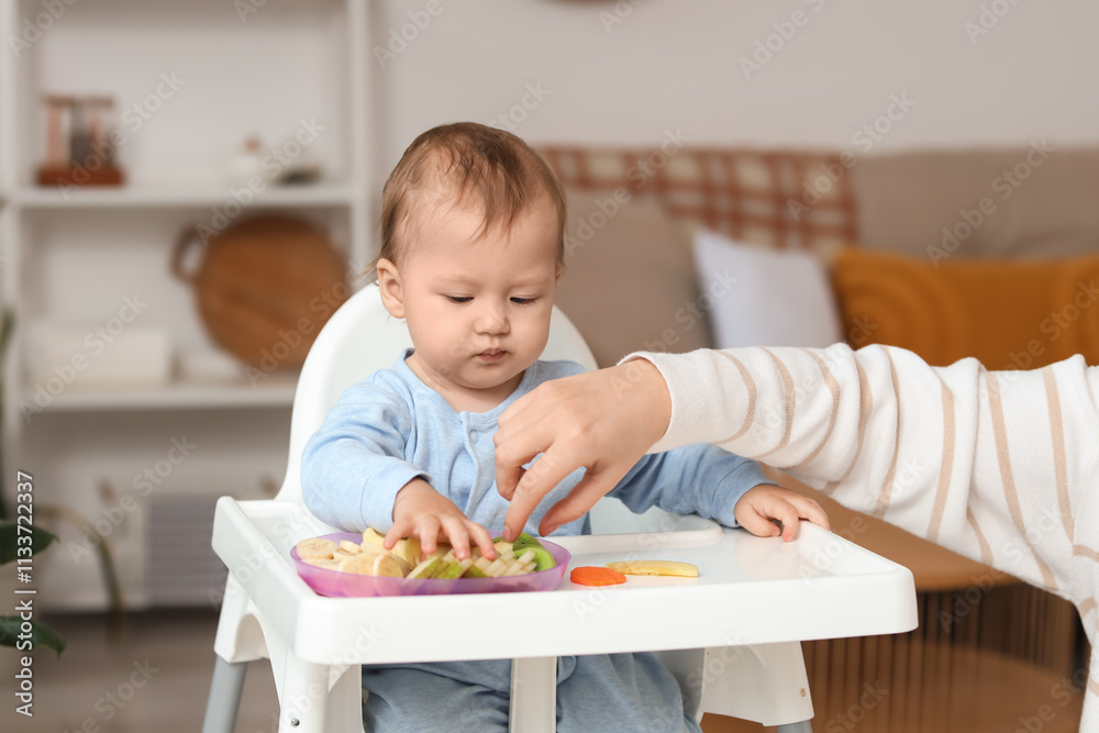 Mother feeding her little baby with fruits in high chair at home Mother feeding her little baby with fruits in high chair at home
