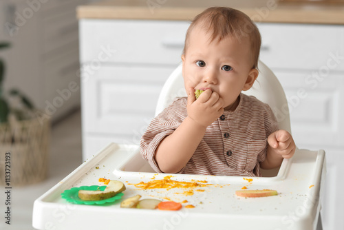 Funny little baby eating in high chair at home