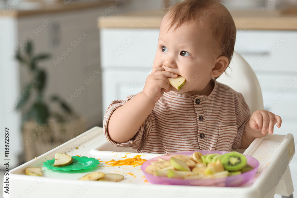 Cute little baby eating pear in high chair at home Cute little baby eating pear in high chair at home