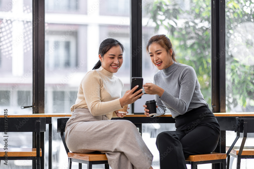 Two asian Female friends drinking coffee and using mobile phones while sitting at cafe
