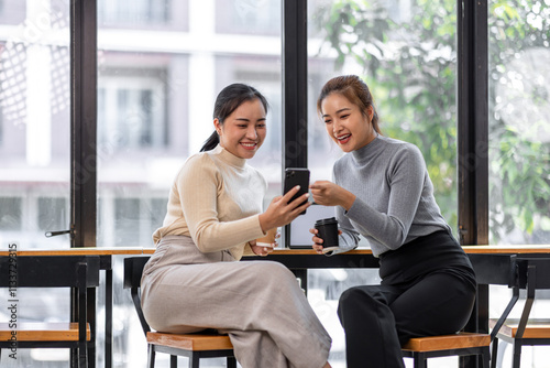 Photography Two asian Female friends drinking coffee and using mobile phones while sitting a