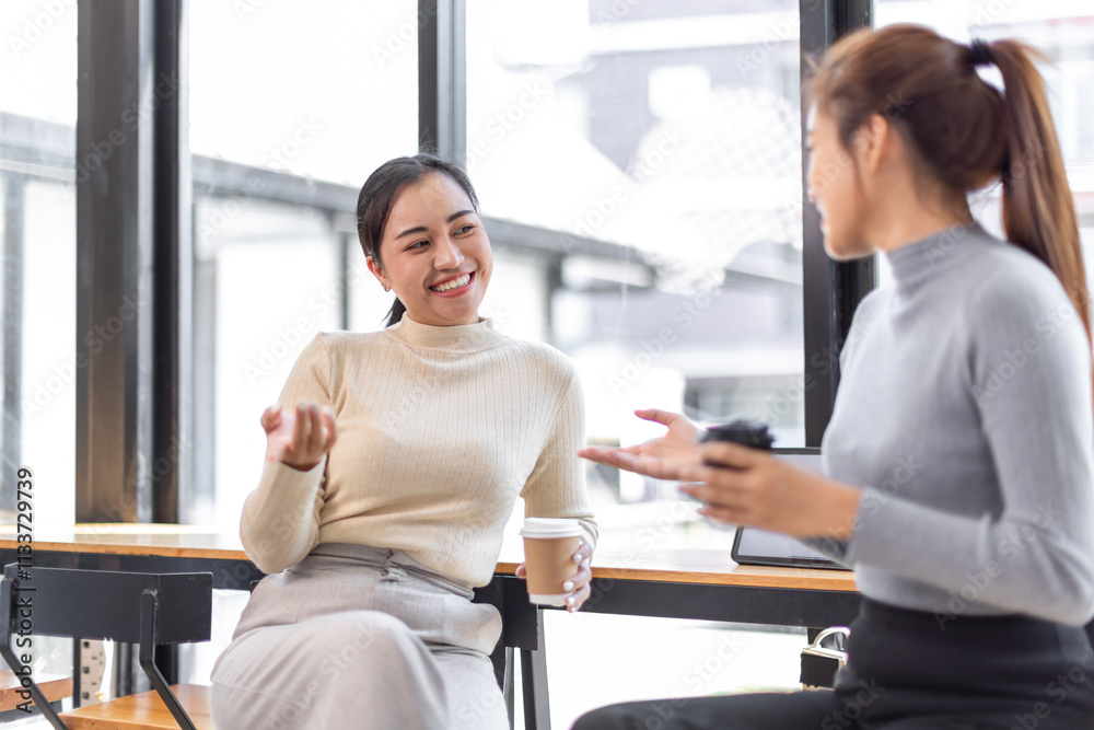 Obraz premium Two asian Female friends drinking coffee and using mobile phones while sitting at cafe 