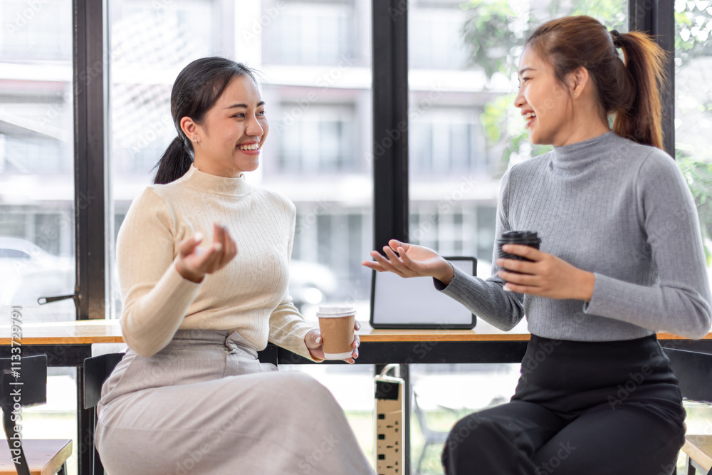 Two asian Female friends drinking coffee and using mobile phones while sitting at cafe
