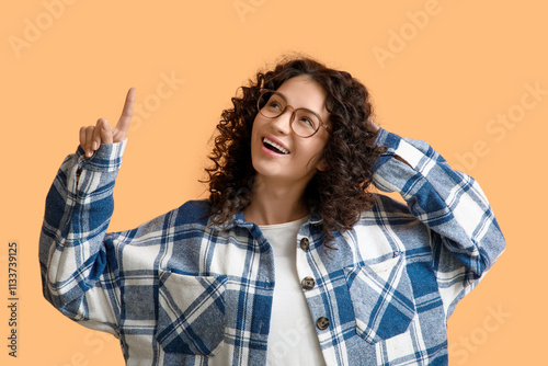 Young woman pointing at something on orange background