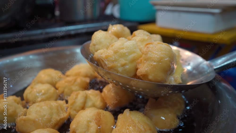 Close-up of a ladle holding golden buñuelos while checking their cooking point. The crispy surface and golden color indicate that they are almost ready to enjoy with honey.