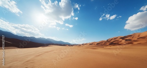 Sunny desert landscape with sand dunes and mountains under a blue sky.