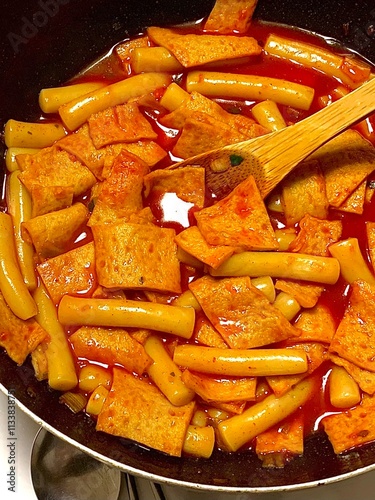 Spicy Korean tteokbokki with chewy rice cakes in a vibrant red sauce, topped with sesame seeds and green onions. A popular street food known for its addictive flavor and satisfying texture.
 photo