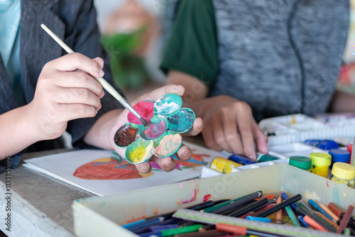 Learning to use poster color to draw various pictures of asian boys on a table outside classroom with his female art teacher, raising teen and adult helps kids school project concept.