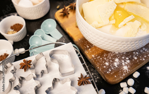preparation for cooking gingerbread cookies figures, eggs, butter and white flour in a bowl, star aniseed and cardamon spices on a black table, wooden cutlery board