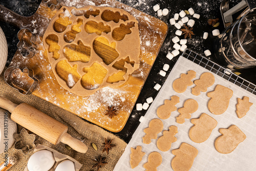 ingerbread dough is rolled out on a wooden board and cut into cookie shapes. Black table as a background, anis star and marshmallow as a decorations
