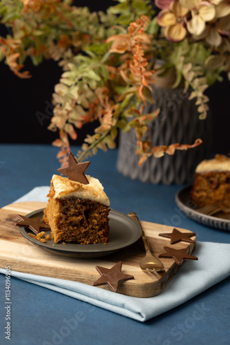 Iced carrot cake sllice served on grey pewter plate with chocolate star and mid blue table cloth, luxury earthy feel