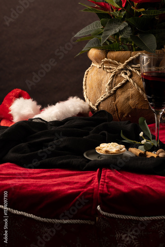 Christmassy scene with rustic fabric rope  pot , santa hat laid on table and red wine - space for copy