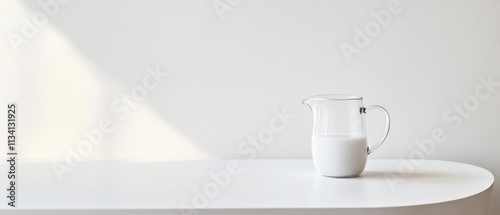 A glass pitcher filled with milk on a minimalist white table against a plain background. photo