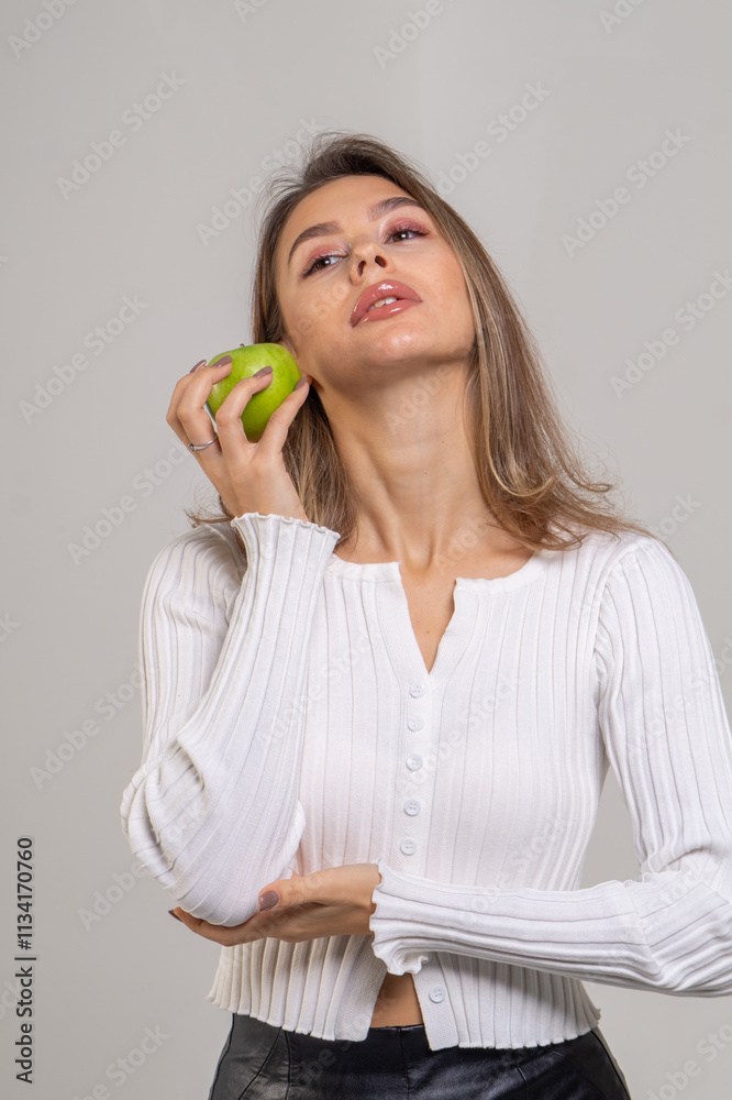 Attractive brunette young woman holding a green apple and standing on a white background. Copy space Attractive brunette young woman holding a green apple and standing on a white background. Copy space