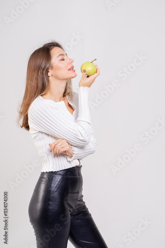 Attractive brunette young woman holding a yellow pear and standing on a white background. Copy space