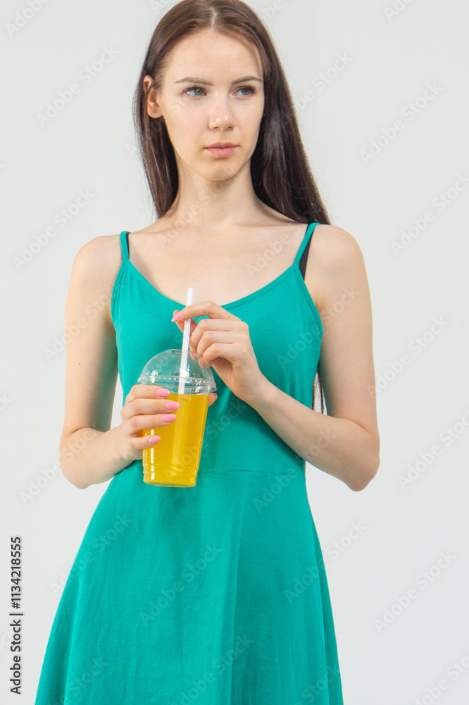 Young attractive girl in a short green dress with a cocktail in her hands on a white background Young attractive girl in a short green dress with a cocktail in her hands on a white background