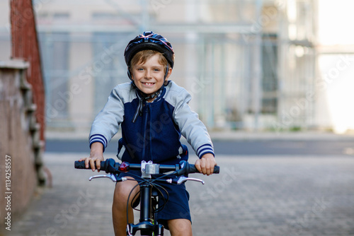 Obraz na płótnie Schoolkid boy in safety helmet riding with bike in the city with backpack. Happy child in colorful clothes biking on bicycle on way to school. Safe way for kids outdoors to school w salonie