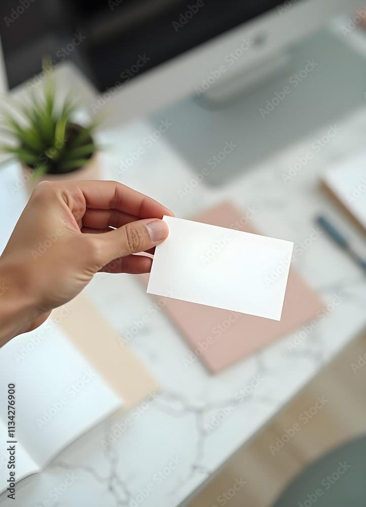 person holds blank business card in modern workspace, surrounded by stationery and plant. clean, minimalistic design creates professional atmosphere person holds blank business card in modern workspace, surrounded by stationery and plant. clean, minimalistic design creates professional atmosphere