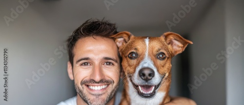 A smiling man poses with his cheerful dog, showcasing a joyful bond between pet and owner in a bright, minimalist setting. photo