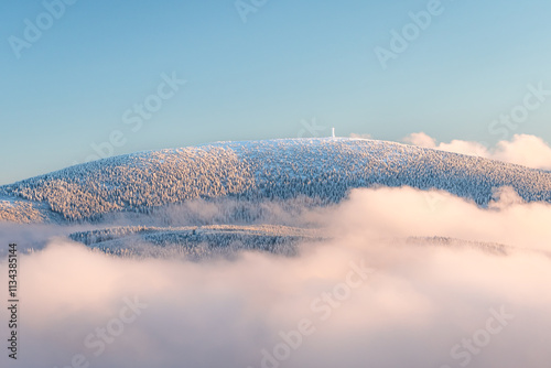 Eastern Sudetes, View of snowy mountain range in fog from hiking trail during winter hike in mountains, viewpoint of wide winter landscape in mountains at sunset.
