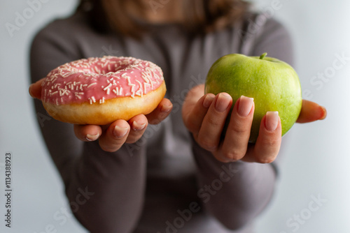 A girl holding an apple and a donut. The choice between healthy eating and junk food
