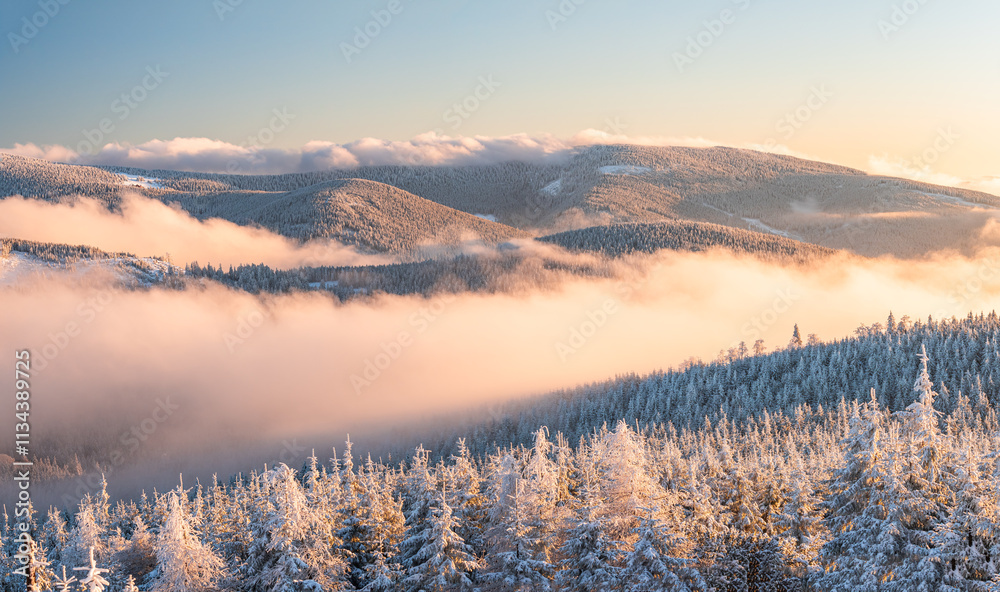 Eastern Sudetes, View of snowy mountain range in fog from hiking trail during winter hike in mountains, viewpoint of wide winter landscape in mountains at sunset.