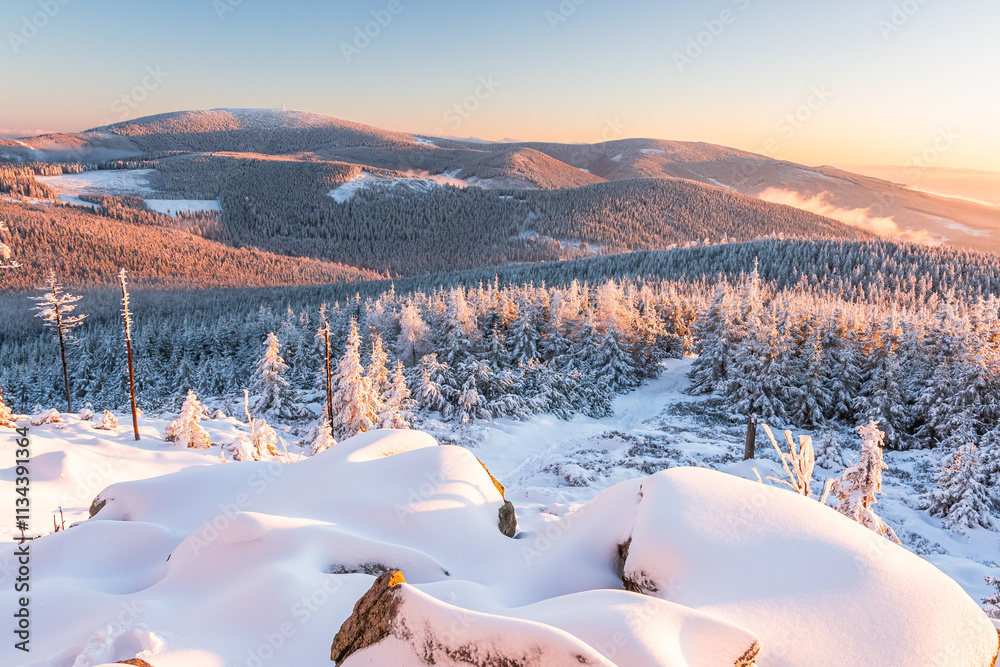 Eastern Sudetes, View of snowy mountain range from hiking trail during winter hike in the mountains, viewpoint of wide winter landscape in the mountains at sunset.