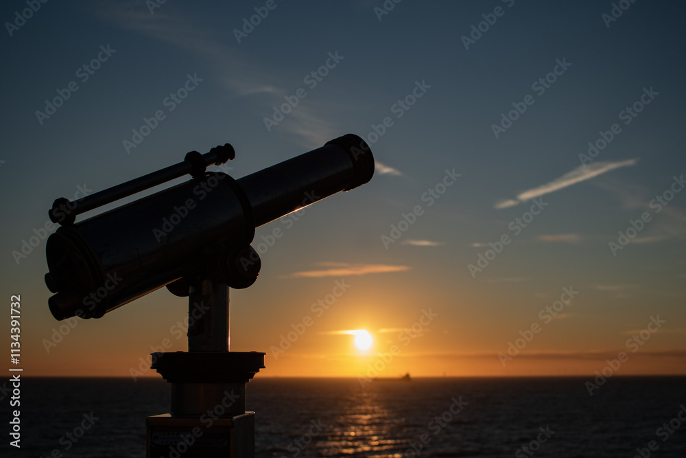 Side view of telescope at the pier in Scheveningen, focus on the foreground, blurred background. Sunset, warm light, tranquil scene. The Hague, Netherlands. Side view of telescope at the pier in Scheveningen, focus on the foreground, blurred background. Sunset, warm light, tranquil scene. The Hague, Netherlands.