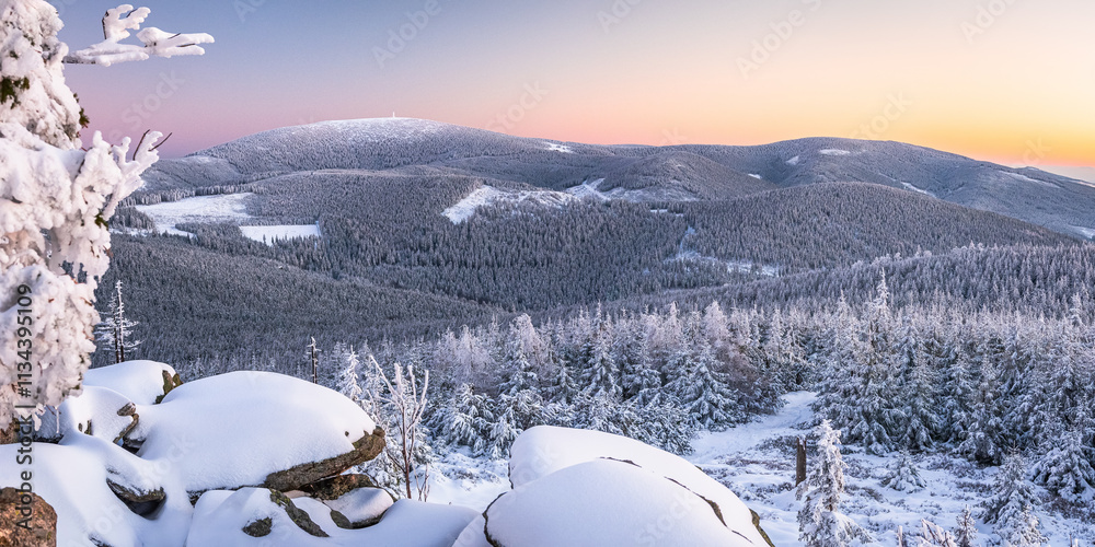 Eastern Sudetes, View of snowy mountain range from hiking trail during winter hike in the mountains, viewpoint of wide winter landscape in the mountains at sunset.