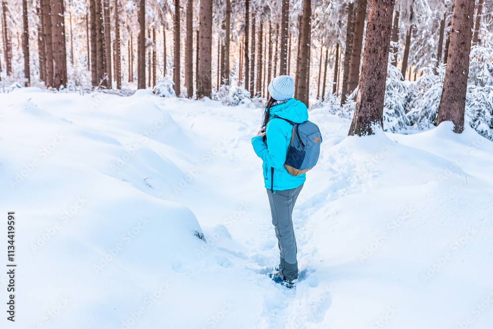 Eastern Sudetes, Young woman hikes on a mountain snow-covered trail, walks on white snow through the forest and looks at the snow-covered trees, winter landscape in the mountains.