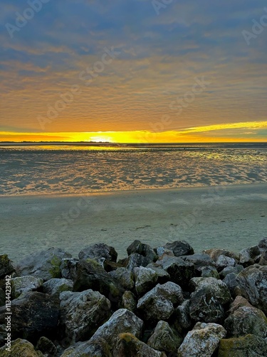 Golden Sunset Over the Bay of Somme Captured from Le Crotoy in October, Reflecting Warm Light on Wet Sand, Rocks, and Vast Low Tide Mudflats Under Dramatic Clouds photo