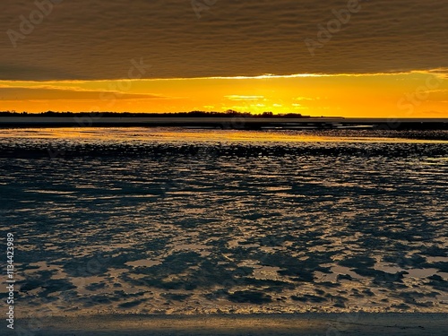 Vibrant Sunset Reflecting on the Bay of Somme’s Mudflats in October, Capturing the Golden Glow, Rippling Tidal Patterns, and a Dramatic Horizon from Le Crotoy photo