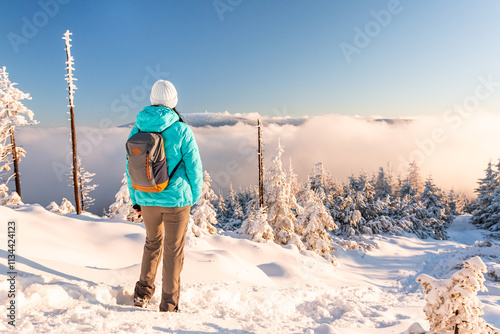Obraz na płótnie Eastern Sudetes, Young woman hikes on mountain snow-covered trail, walks on white snow over snowy peak and looks at fog in valley, winter landscape in mountains on sunny day. w salonie