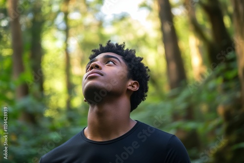 Young man gazes upward, forest backdrop.