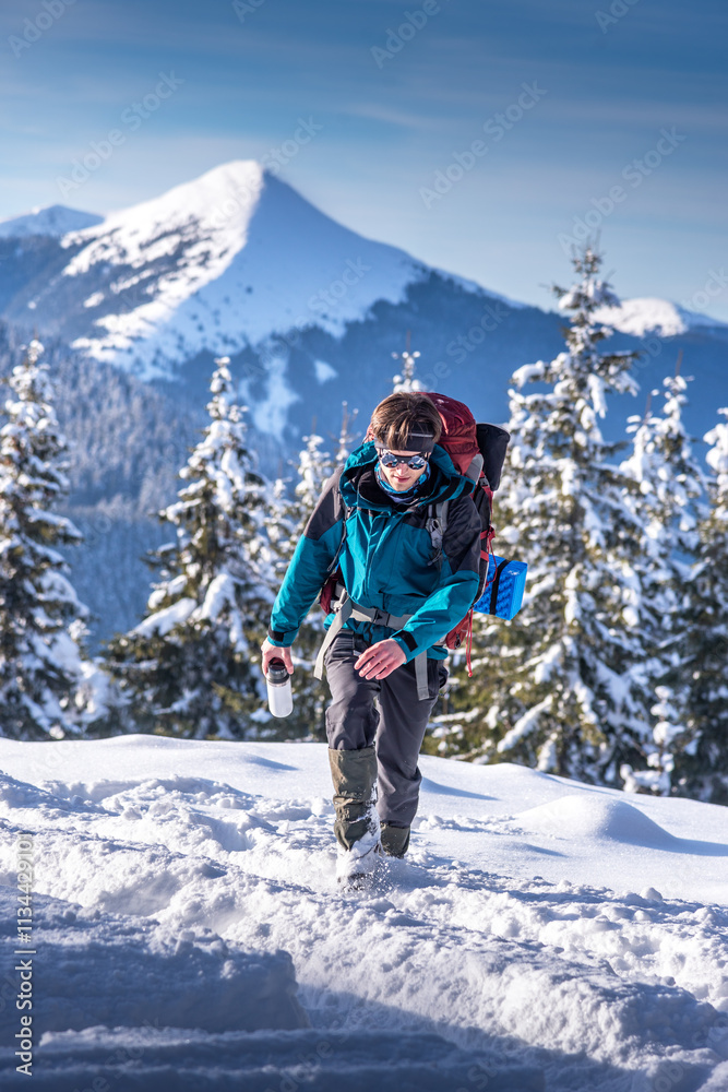 Young backpacker hiking in snowy mountain area with reusable travel mug, against a scenic backdrop of snowy mountains Young backpacker hiking in snowy mountain area with reusable travel mug, against a scenic backdrop of snowy mountains