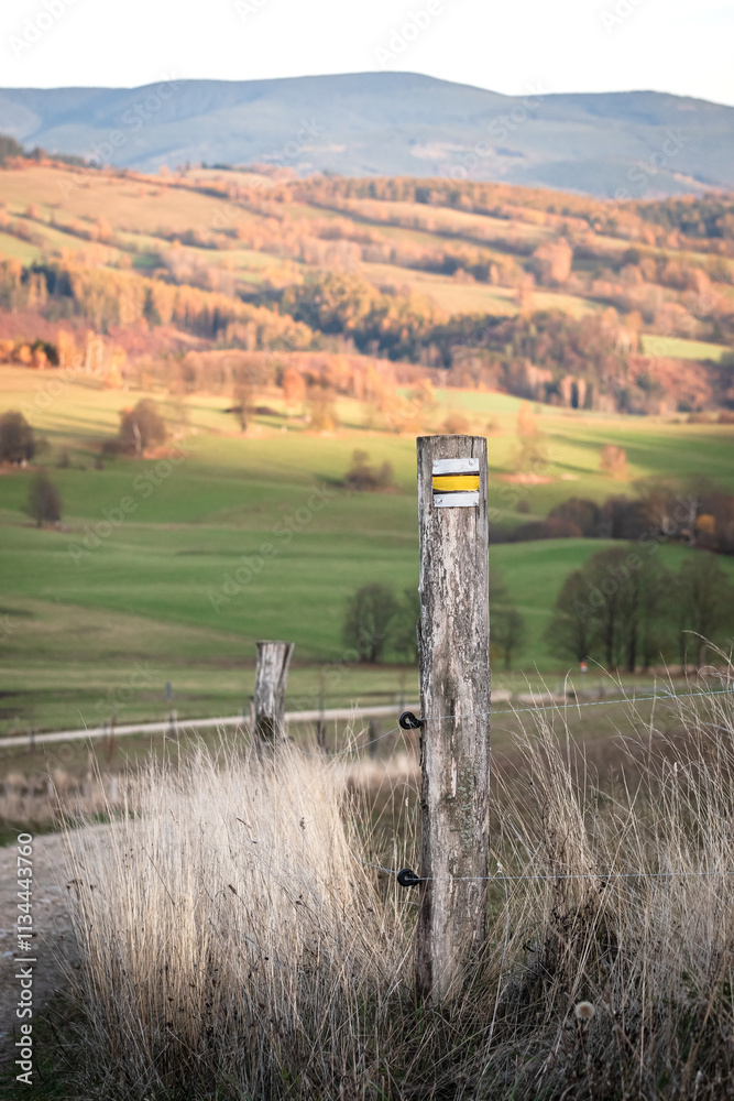 Czech Republic, Stribrnice, yellow hiking trail marking on a post. Autumn panorama of hills and fields, view from the hiking trail in the late evening.