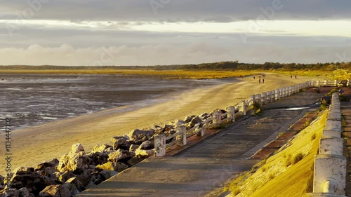People Strolling Along the Beach in Le Crotoy at Sunset, Surrounded by Golden Light, Coastal Rocks, and Scenic Views of the Bay of Somme photo