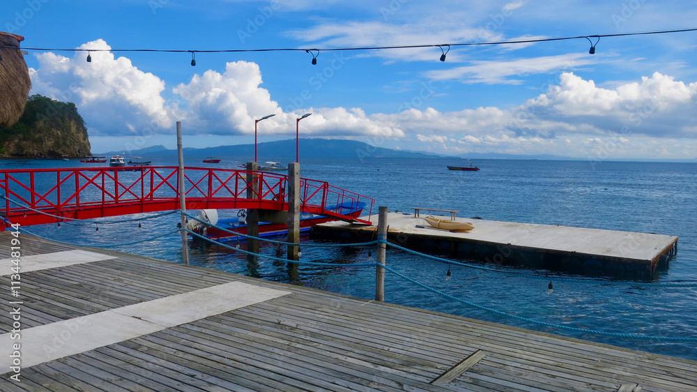 Obraz premium View of a pier on the shore of a tropical island. A boat dock with a wooden deck and a small bridge connecting the pier and a floating platform.