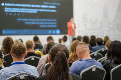 People gathered in a conference hall attending a business seminar with a speaker on stage.