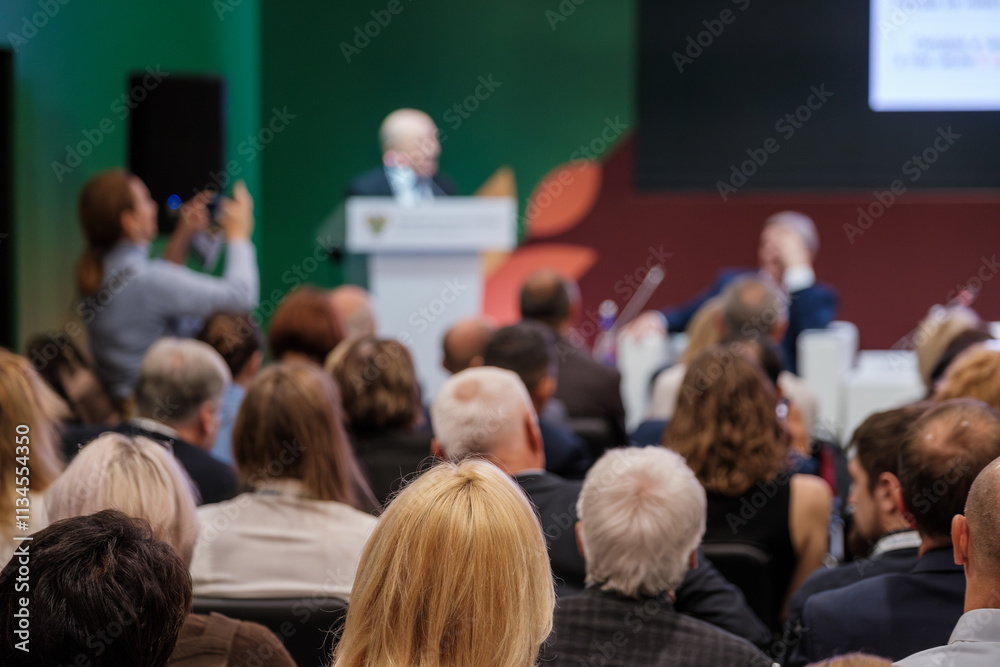 Large audience attending a professional seminar in an auditorium, focusing on speaker's presentation.