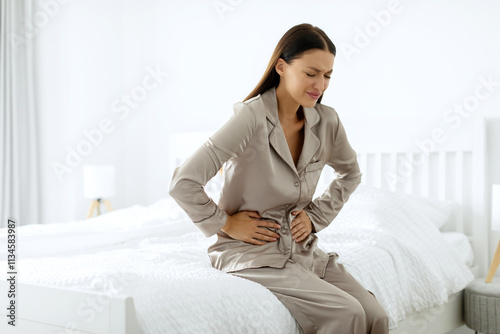 Foto Lady feeling stomach pain in the morning, sitting on bed and touching belly, hav