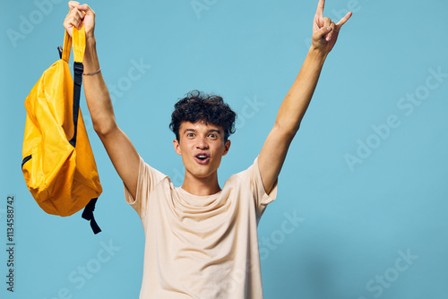 Young man celebrating with a yellow backpack, vibrant blue background, energetic pose, expressing excitement and joy Perfect for concepts related to happiness, success, or youth culture photo