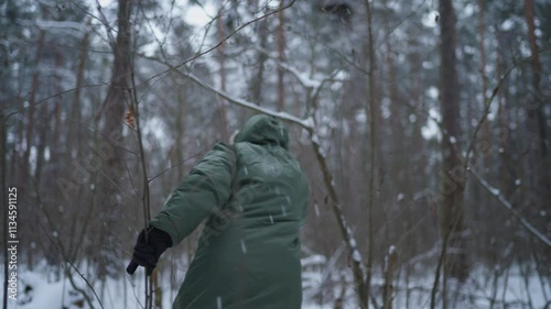 a man in a green jacket walks through the winter forest