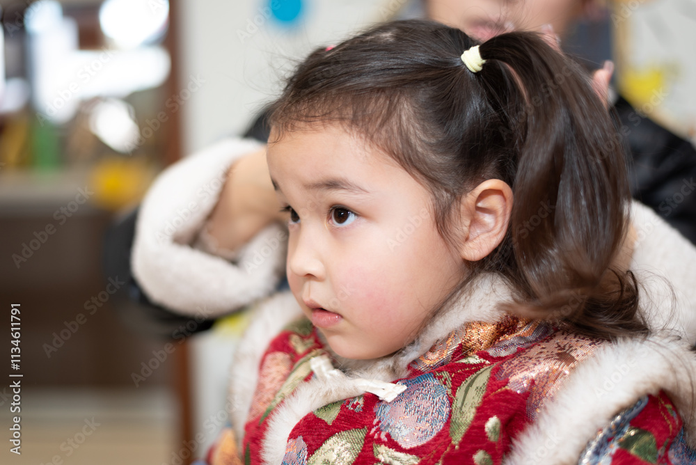 The young Chinese mother is combing and binding her daughter's hair. Her daughter is wearing traditional Chinese clothes. They're getting ready for celebrating Chinese New Year. The young Chinese mother is combing and binding her daughter's hair. Her daughter is wearing traditional Chinese clothes. They're getting ready for celebrating Chinese New Year.