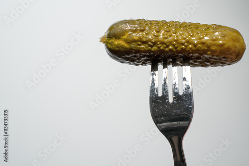 Delicious cucumber fresh from the jar on a shiny fork. White space.