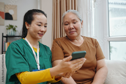 Social worker showing medical application on mobile phone to old woman