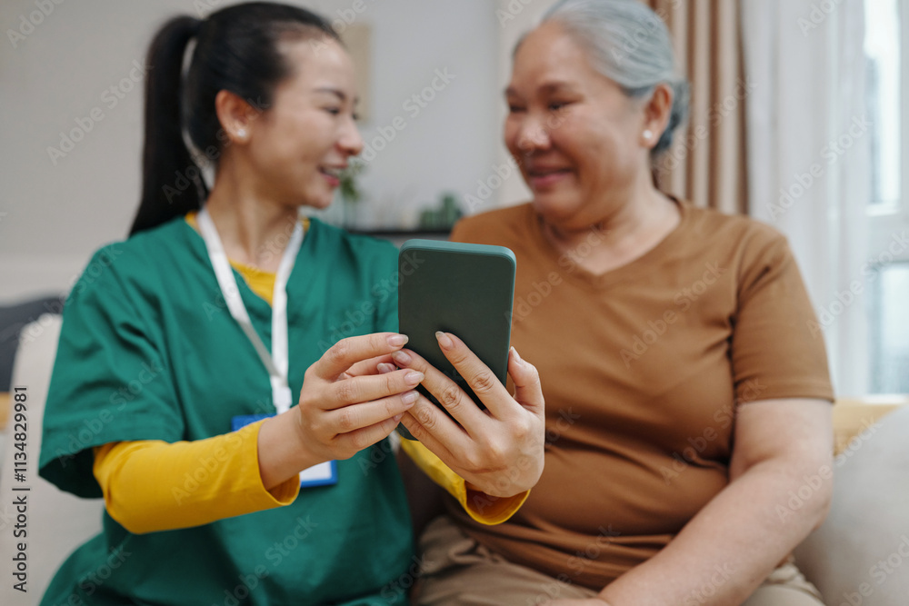 Nurse showing apps in mobile phone to senior woman while they sitting in the room Nurse showing apps in mobile phone to senior woman while they sitting in the room